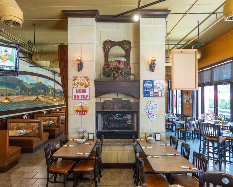 Restaurant interior with a stone fireplace, booths, tables, and a mural of a landscape.