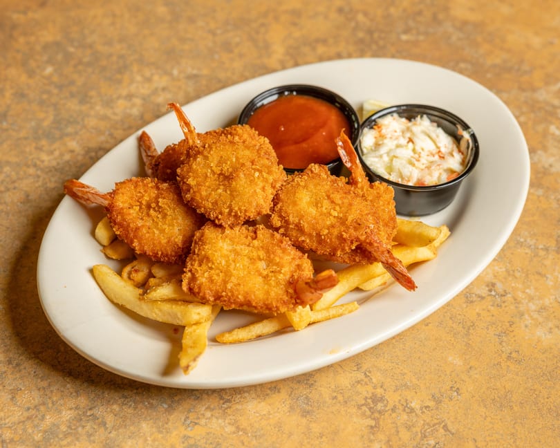 A plate of golden-brown fried shrimp and french fries, with sides of coleslaw and cocktail sauce.