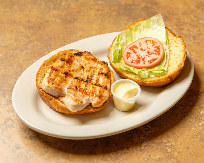 Grilled chicken sandwich on a bun with lettuce, tomato, and a side of mayonnaise.