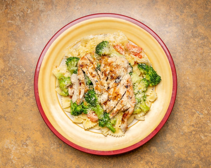 Grilled chicken and broccoli farfalle pasta with parmesan cheese on a yellow plate.