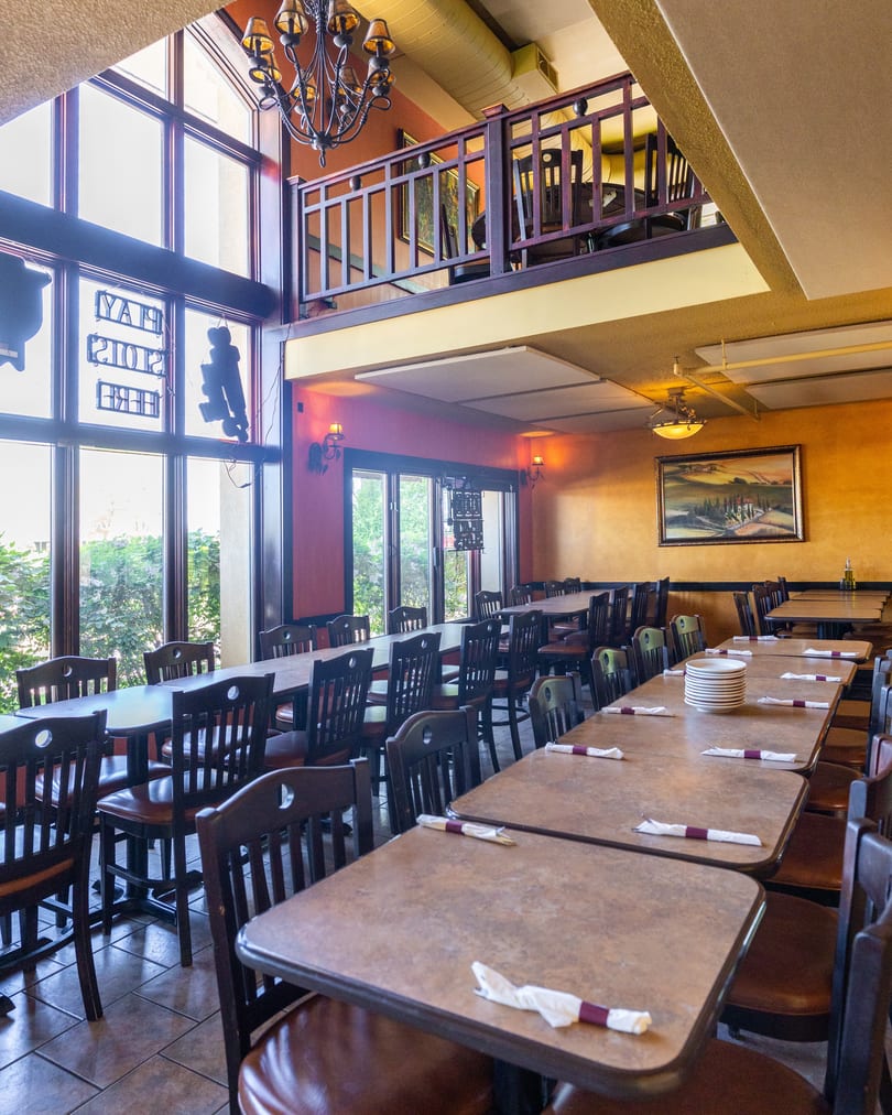 Spacious restaurant dining room with tables, chairs, large windows, and an upper-level seating area.