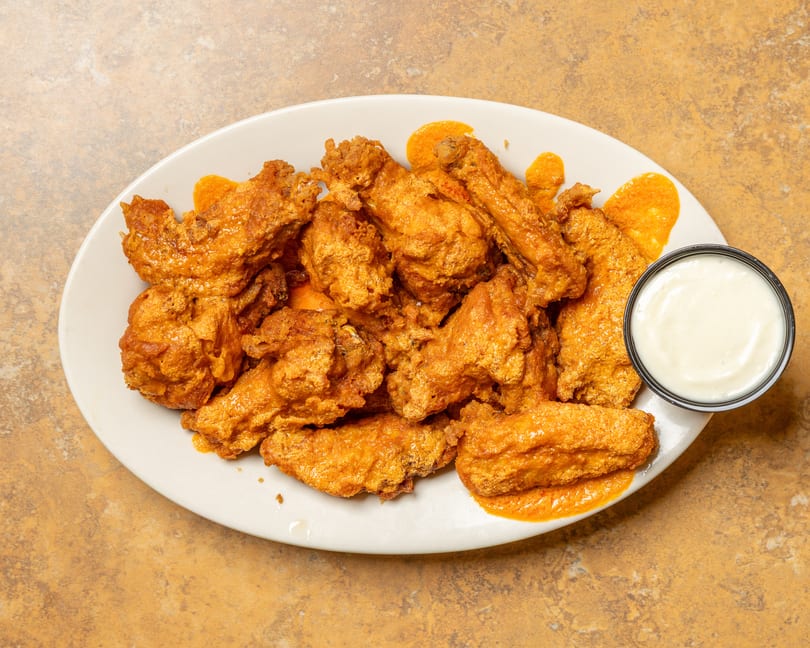 A white oval plate filled with crispy, orange-glazed chicken wings and a side of ranch dressing.