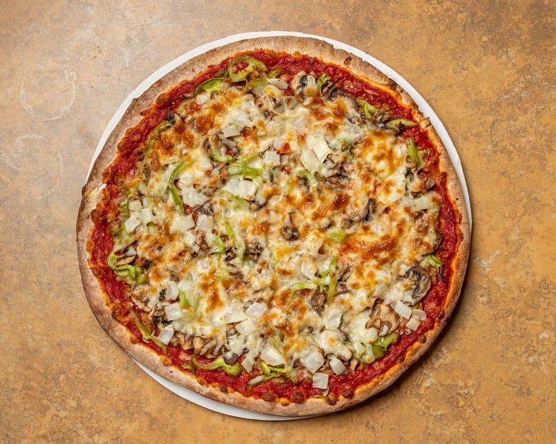 A whole pizza with melted cheese, green peppers, onions, and mushrooms on a white plate.