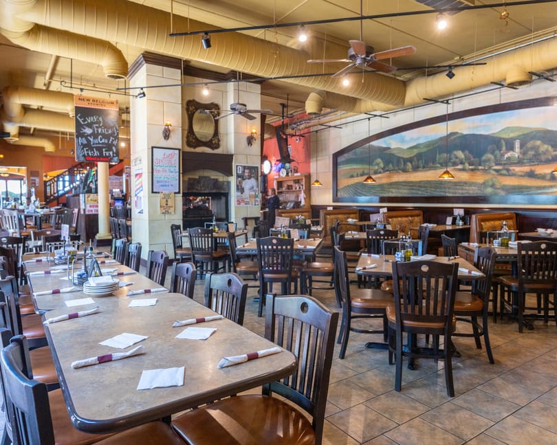 Spacious restaurant interior with multiple dining tables, chairs, and a large landscape mural on the wall.