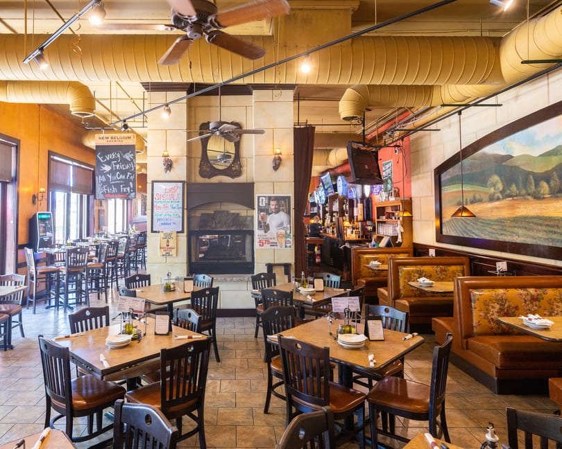Interior of a restaurant with tables, chairs, booths, a bar, and a fireplace.