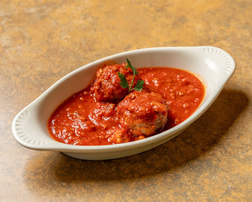 Two meatballs covered in red sauce and garnished with parsley in a white dish.