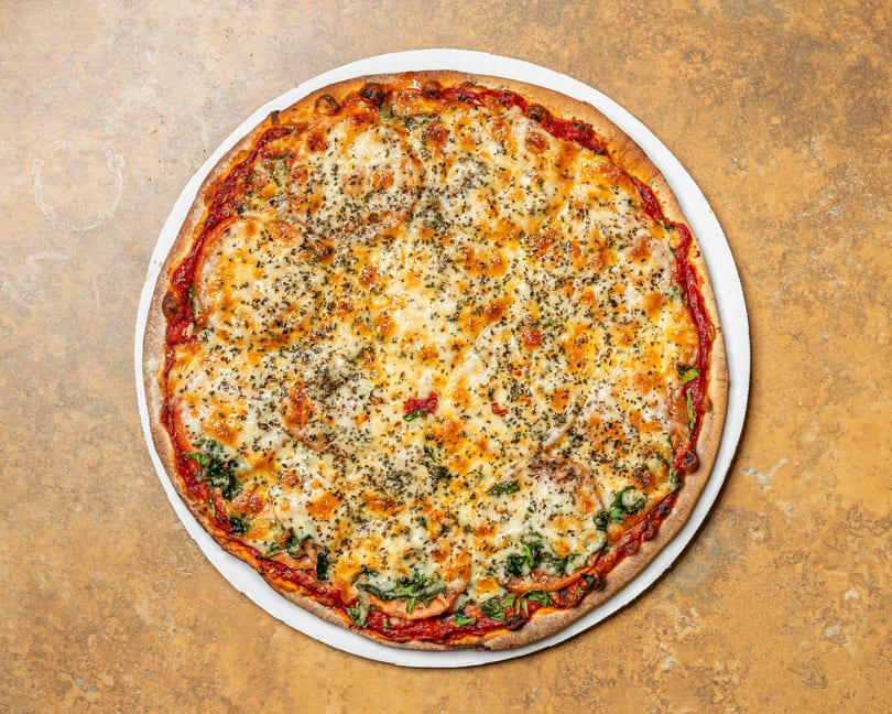 A whole, round pizza with melted cheese, tomato slices, and green herbs on a white plate.