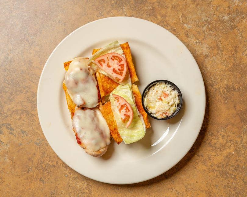 Open-faced sandwiches with melted cheese, lettuce, and tomato, served with a side of coleslaw.